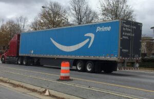 Truck with blue Amazon trailer is parked by an orange traffic cone.